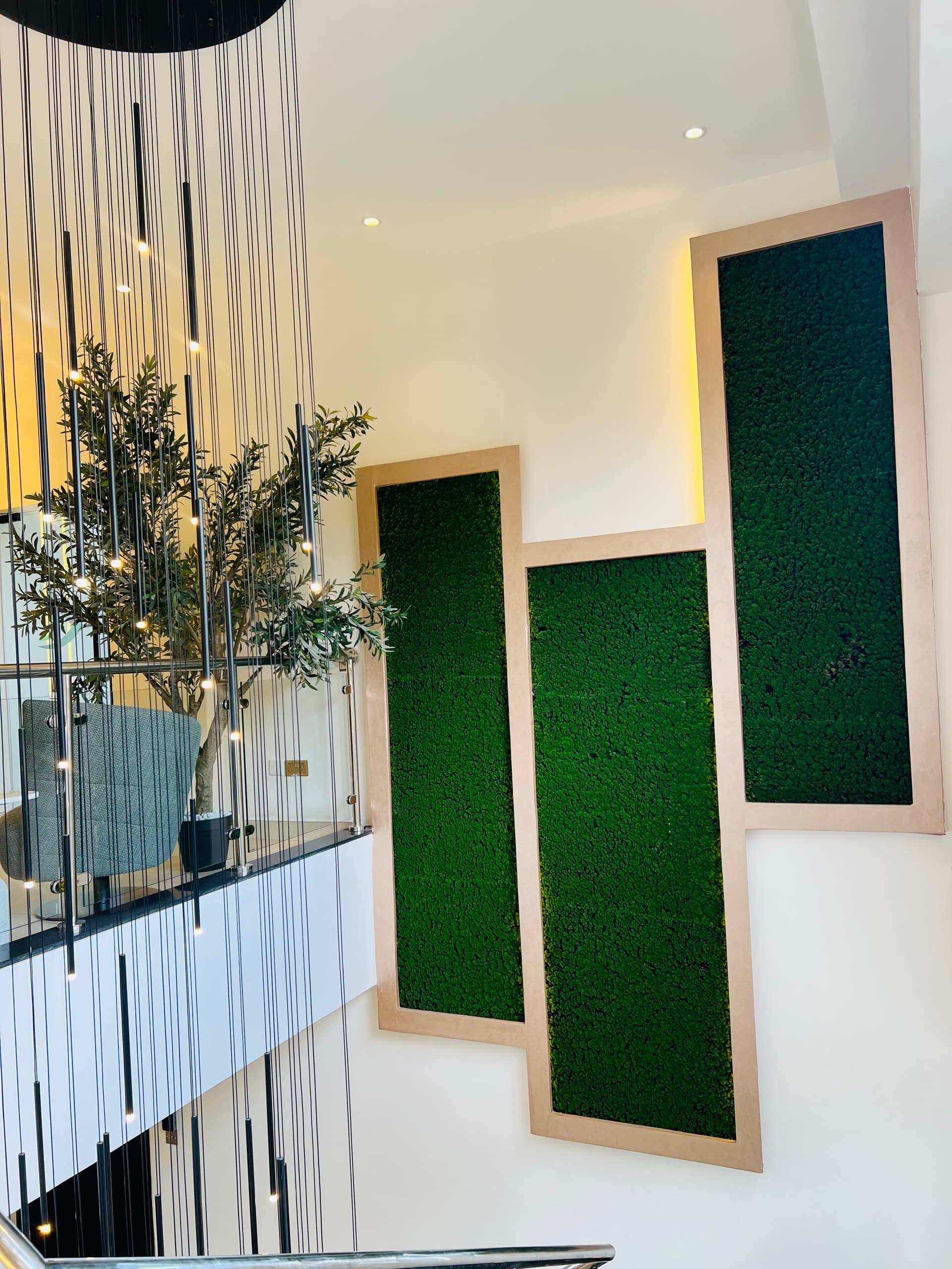 Preserved moss panels and cascading filament pendants at the staircase void
